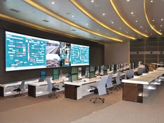 an office with multiple computer screens on the wall and desks in front of them