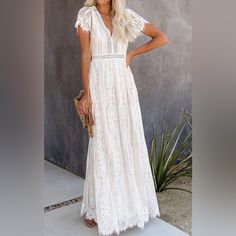 a woman in a long white dress standing next to a plant and holding a purse