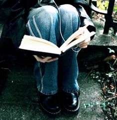 a person sitting on a bench reading a book with headphones attached to their ears