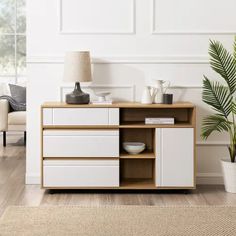 a living room with white furniture and a potted plant on the sideboard next to it