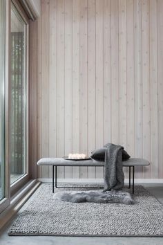 a bench sitting on top of a rug in front of a window next to a wooden wall