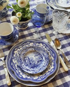 a table set with blue and white dishes, silverware and flowers in vases