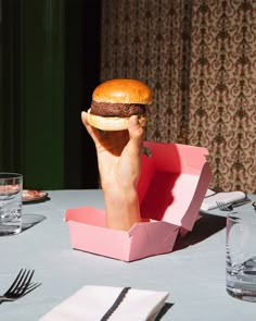 a person holding up a large hamburger in front of their face at a dinner table