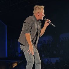 a man standing on top of a stage while holding a microphone in his right hand