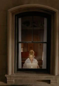 a woman sitting in front of a window with a laptop computer on her lap and looking out the window