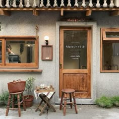 two wooden stools sitting in front of a building with windows on each side and a sign above the door