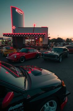 several cars parked in front of a building with a neon sign on it's side