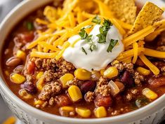 a white bowl filled with chili and cheese topped with sour cream, tortilla chips