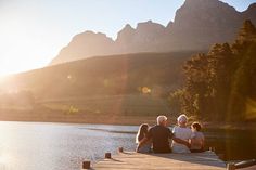 three adults and two children sitting on a dock overlooking a lake with mountains in the background