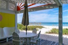 an outdoor table and chairs on a wooden deck near the beach with an umbrella over it