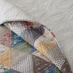 an up close view of a quilt on a bed with white sheets and colorful patterns