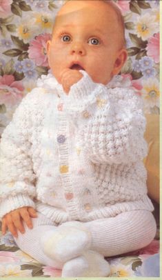 a baby is sitting on a floral chair wearing a white sweater and pants with buttons