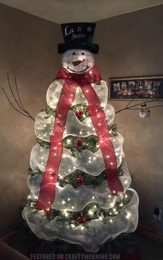 a lighted christmas tree with a snowman top hat and red ribbon on it's head