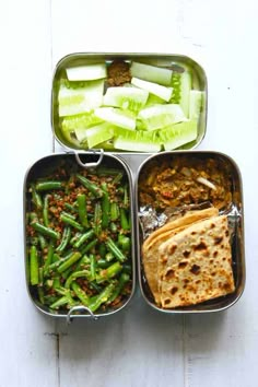 three metal trays filled with food on top of a white wooden table next to each other