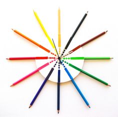 a clock made out of colored pencils on a white surface