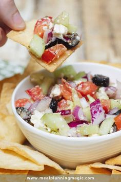 a hand holding a tortilla chip over a bowl of salad