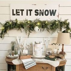 a christmas mantle with garland and lights on it, next to a sign that says let it snow