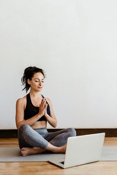 a woman sitting on the floor with her laptop in front of her, doing yoga