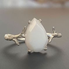 "For fans of minimalist nature-inspired jewelry, we created our stand-out Mother Nature Silver breastmilk ring. It pairs together a branch-like sterling silver ring band with an exquisite yet small pear-shaped faceted breastmilk stone. Go with your natural breast milk or combine your breast milk with opal effect flakes or pearl powder. Opalizing your breast milk adds a pale, milky opal appearance to your breastmilk stone that catches the light and reflects pastel rainbow hues, while adding pearl White Adjustable Nature-inspired Jewelry, Delicate White Moonstone Ring For Anniversary, White Sterling Silver Nature-inspired Jewelry, Nature-inspired White Sterling Silver Jewelry, Delicate Handmade White Rings, White Teardrop Moonstone Ring In Sterling Silver, Delicate White Moonstone Ring In Sterling Silver, Unique White Moonstone Jewelry, Minimalist White Moonstone Ring In Sterling Silver