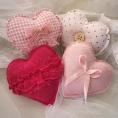 three heart - shaped cushions are sitting on a lace tablecloth, one has a button and the other has a bow