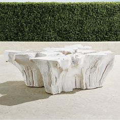 a table made out of wood sitting on top of a cement ground next to a hedge