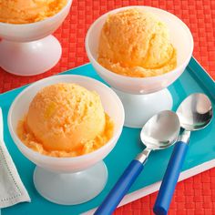 two bowls filled with orange ice cream on top of a blue tray next to spoons