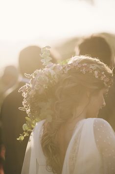 a woman in a white dress with flowers on her head and people standing behind her