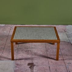 a small wooden table sitting on top of a tile floor next to a green wall