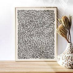 a vase with some dried plants in it next to a framed art print on a wall