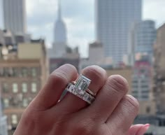 a woman's hand holding an engagement ring in front of a cityscape