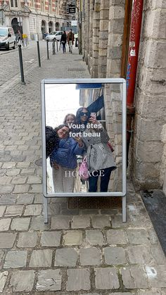 a sign on the side of a brick road with people taking pictures in front of it