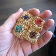 a hand holding four small gold filigrees