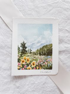 a watercolor painting of flowers and trees on a white paper with a ribbon around it