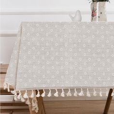 a white table cloth with tassels and flowers in a vase on the side