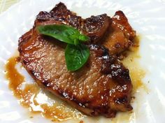 a piece of meat on a white plate with sauce and green leaf garnish