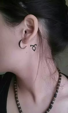 a woman with a black and white tattoo on her left ear is wearing a necklace