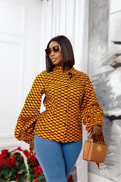 Make a statement in the ELIZA African Print Puff Sleeve Shirt! Perfect for the office or your next event, this top can be worn with a skirt, pants or jeans for a stylish look appropriate for any occasion. Rock this trend-worthy piece and keep your style up-to-date for the season. FEATURES.* 100% African Wax Cotton* Tied-Puff sleeve design* Unlined Button up shirt.* Model Is Wearing A Size Medium and 2X-Large.CARE INSTRUCTION* Hand Wash in Cold Water.* Do Not Bleach.* Press with Cool Iron on The African Shirt And Trouser For Women, African Print Skirt And Top For Office, African Shirts For Ladies, African Print Tops With Jeans, Ankara Top Styles For Jeans, African Print Tops Blouses, Ankara Tops With Jeans, Ankara Tops Blouses, Ankara Top Styles