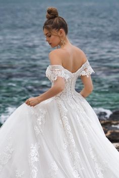 a woman in a white wedding dress standing on the rocks by the ocean with her back to the camera