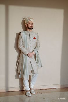 a man standing in front of a wall wearing a white suit and turban