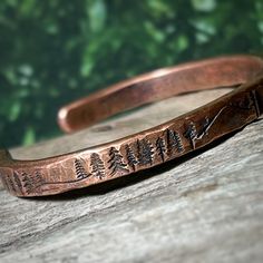 A rustic handmade bracelet that celebrates the beauty of nature and the majesty of the forest with the mountains and trees hand stamped around the rustic copper cuff.   Perfect for the mountain climber or hiker in your life.  This engraved copper bracelet is hand forged and finished with a hammered finish to give it a rustic look, perfect for men and women alike.  Each bracelet is handmade, and no two will be exactly alike. Also please be aware that colors may vary due to viewing screens. If you Unique Cheap Copper Jewelry, Mens Copper Bracelet Western, Handmade Copper Jewelry Turquoise, Cheap Copper Jewelry For Women, Cheap Copper Jewelry, Cheap Rustic Jewelry For Gifts, Cheap Rustic Jewelry For Gift, Luxury Artisan Copper Jewelry, Cheap Hypoallergenic Copper Jewelry