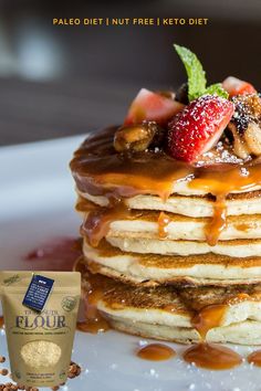 a stack of pancakes covered in syrup and fruit with a bag of granola next to it