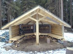 a small wooden shelter in the middle of snow covered ground with logs stacked around it