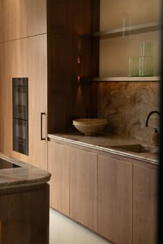 a modern kitchen with wooden cabinets and marble counter tops, including a bowl on the sink