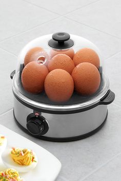 an egg cooker with six eggs in it on the counter next to two plates