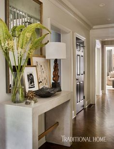 a vase with flowers on a table in front of a mirror and door to another room