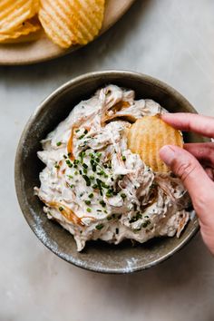 a person holding a cracker over a bowl of coleslaw and potato chips