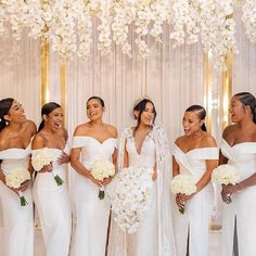 a group of women standing next to each other in front of a white wall with flowers