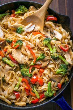 a skillet filled with pasta and vegetables on top of a wooden table next to a blue towel