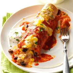 an enchilada on a white plate with a fork and napkin next to it