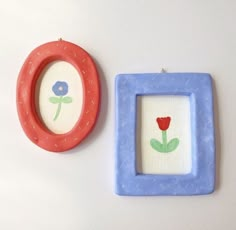 two small frames with flowers painted on them next to each other, one red and one blue